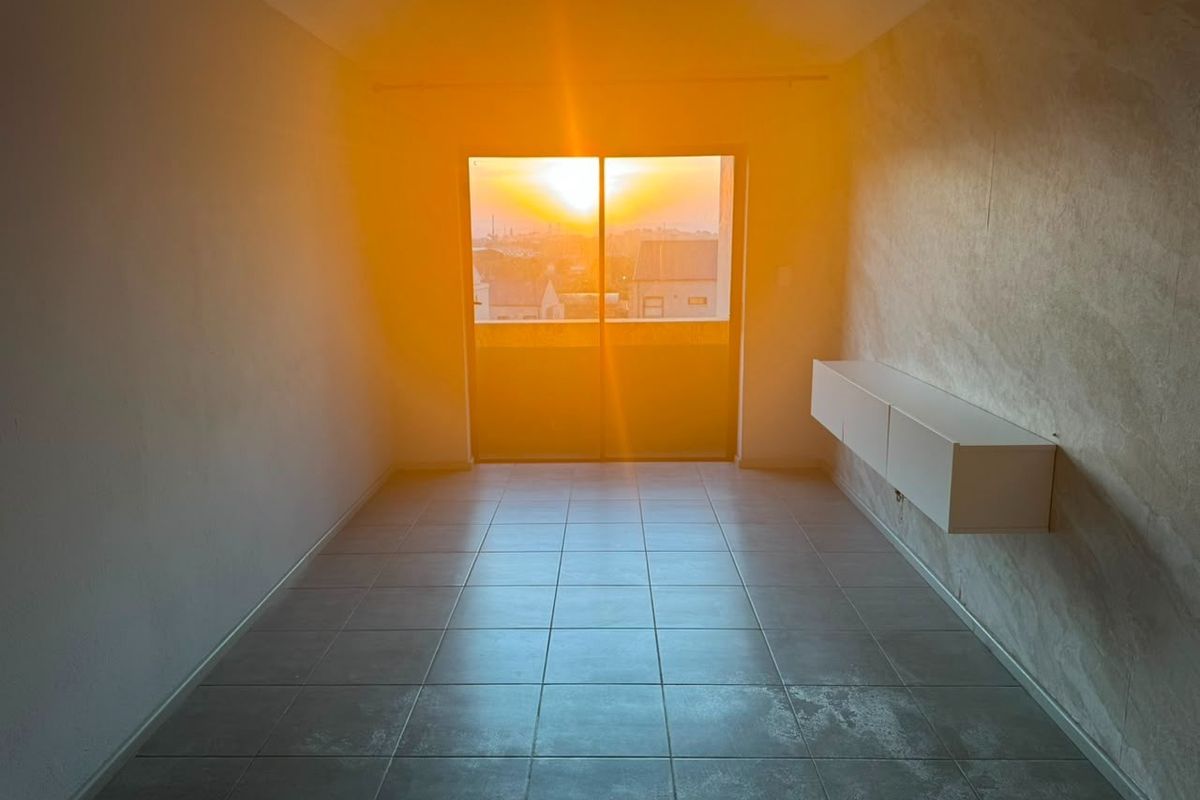 An empty living room featuring tiled flooring, wall-mounted storage, and a sliding glass door leading to a balcony with sunset views.