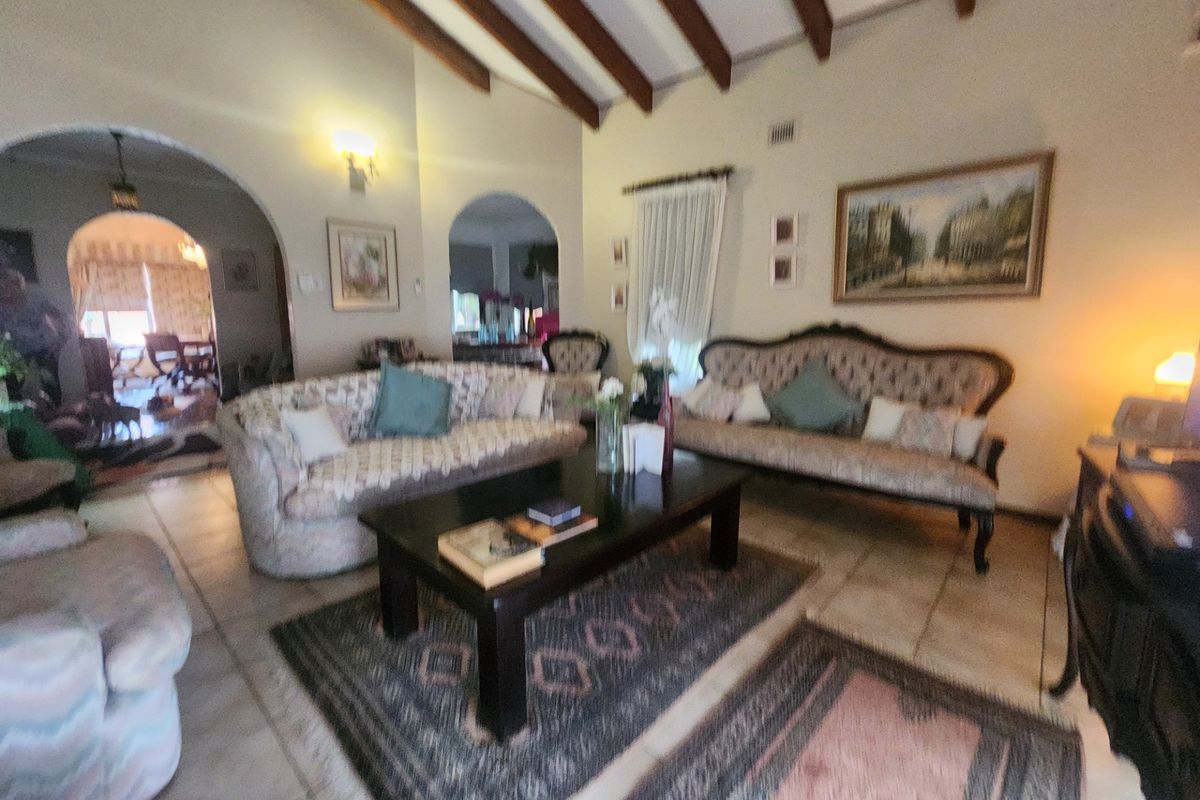 Spacious living room featuring exposed timber ceiling beams, tiled flooring, and classic arched doorways leading to adjacent living areas.