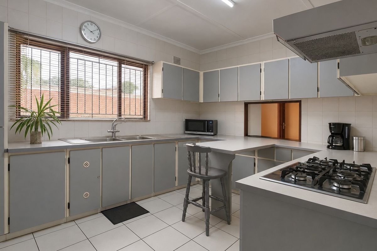 A functional kitchen featuring grey built-in cabinetry, a gas hob with extractor fan, stainless steel sink, and tiled finishes throughout.
