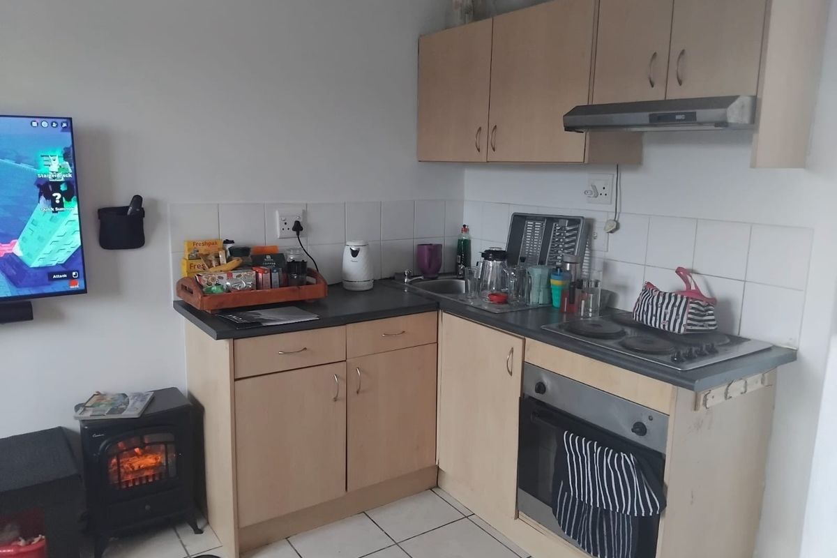 Compact kitchen featuring laminate cabinetry, built-in oven, electric hob, extractor fan, and tiled splashbacks with ceramic floor tiles.