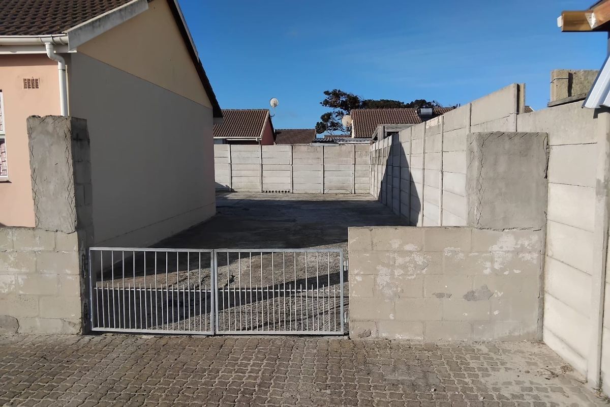 A vacant rear yard area featuring a concrete slab, enclosed by precast concrete boundary walls and secured with a metal gate.