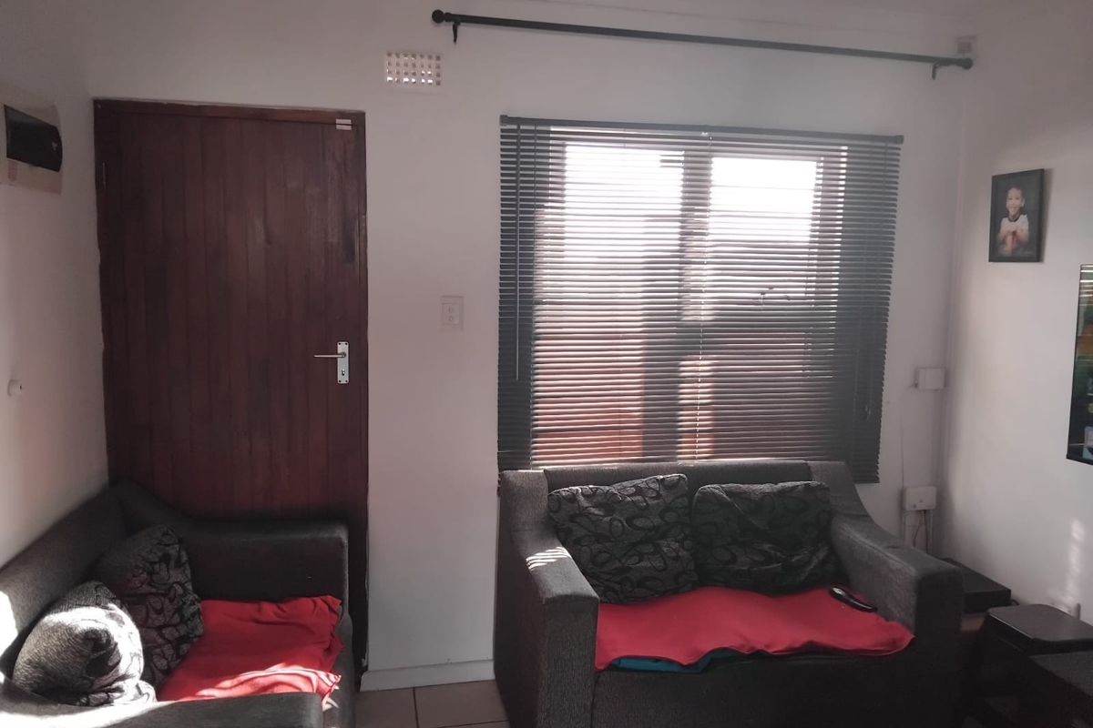 A living room area featuring tiled flooring, a timber door, and venetian blinds on the window.