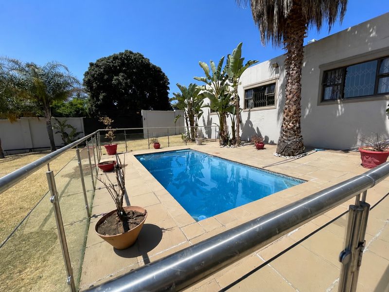 Outdoor pool area featuring a rectangular swimming pool, tiled surround, and modern glass balustrade with stainless steel handrails.