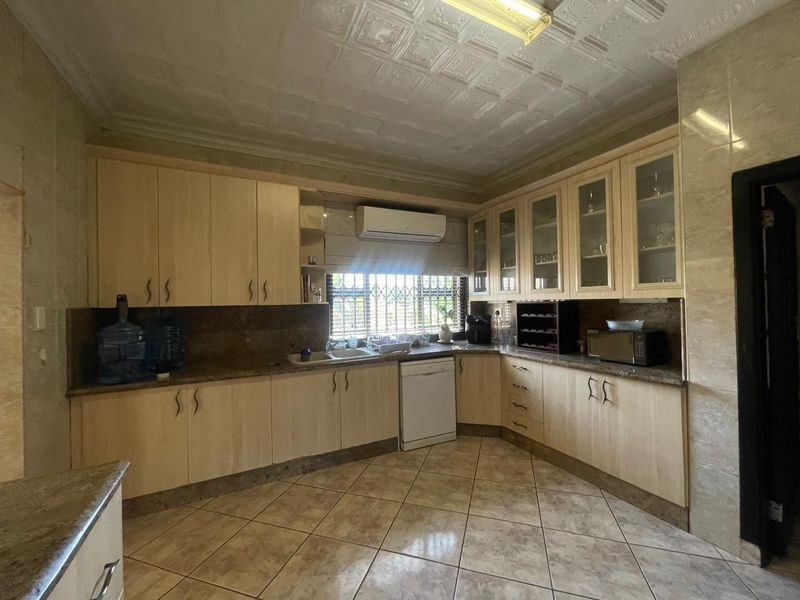 A functional kitchen featuring light wood cabinetry, stone countertops, tiled flooring, and decorative ceiling tiles, equipped with a split-system air conditioner.