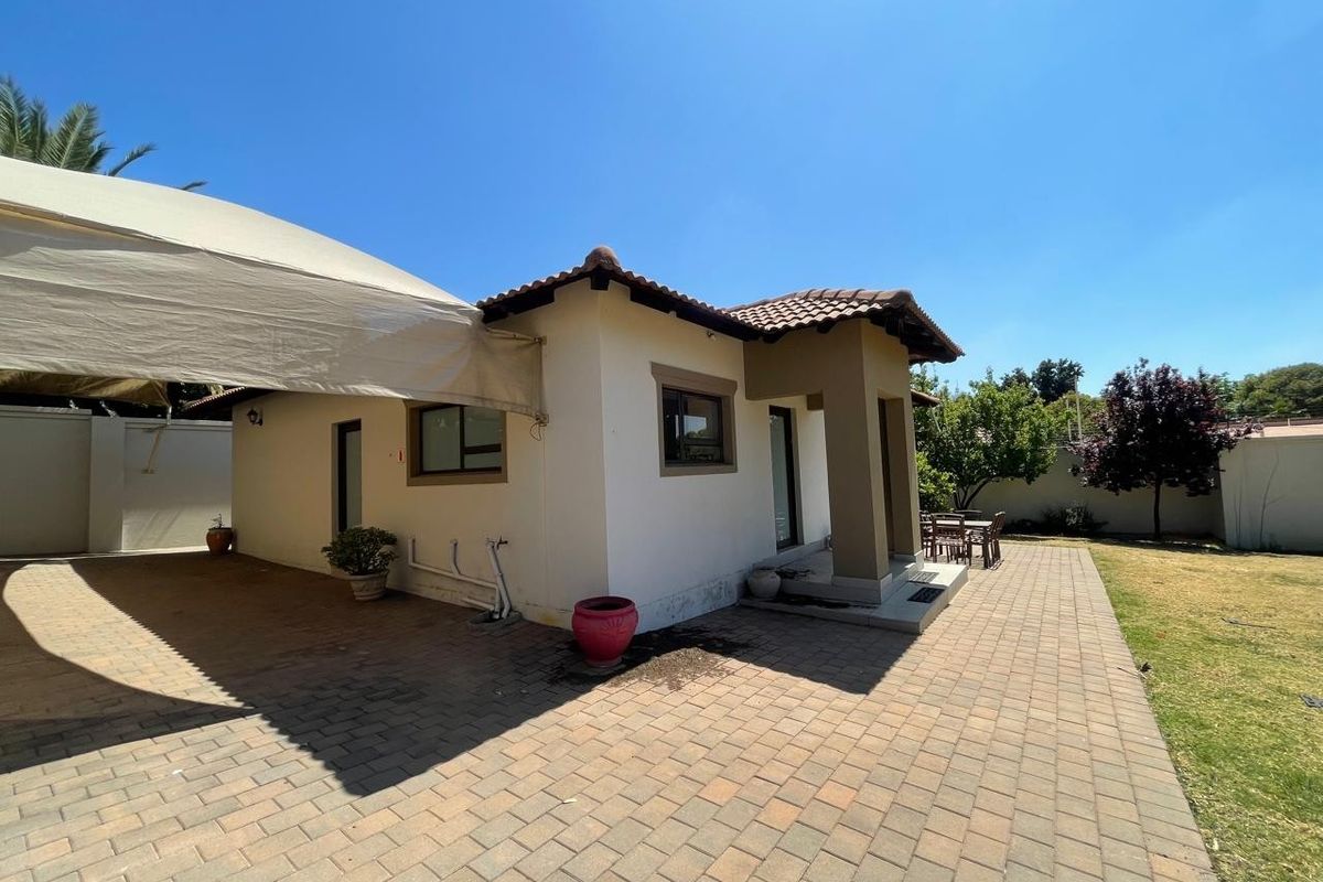 Rear view of the property featuring a paved patio area, a large shade sail, and a well-maintained garden with boundary walls.