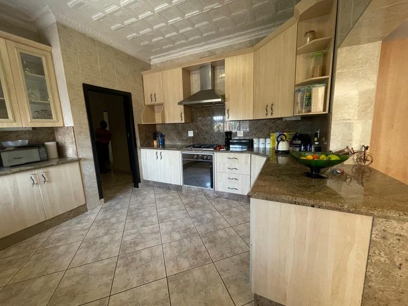 A functional kitchen featuring granite countertops, light wood cabinetry, built-in oven with gas hob, and tiled finishes throughout.