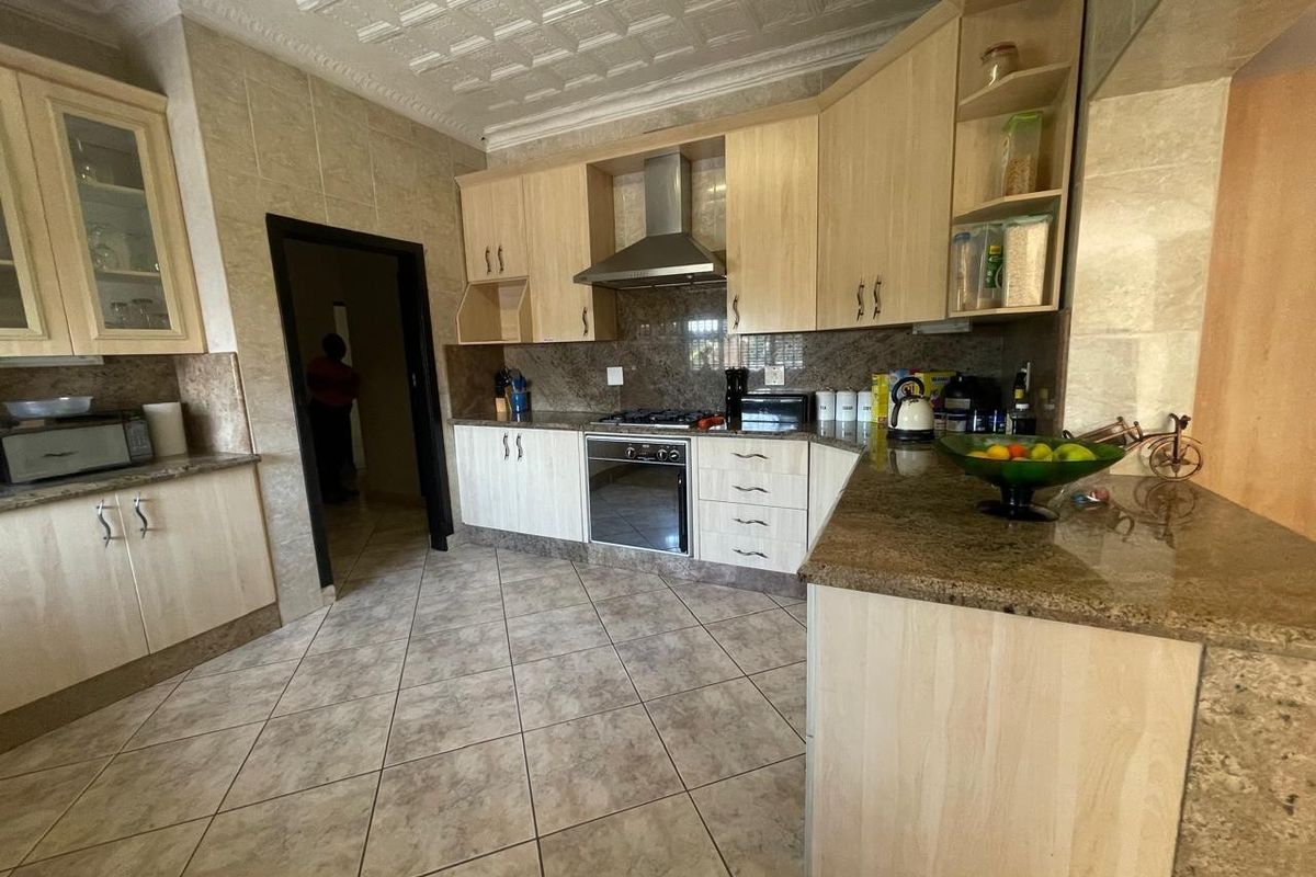 A functional kitchen featuring granite countertops, light wood cabinetry, built-in oven with gas hob, and tiled finishes throughout.