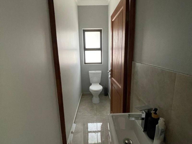 A compact guest bathroom featuring a wall-mounted basin with a modern mixer tap and a separate toilet area with tiled flooring.