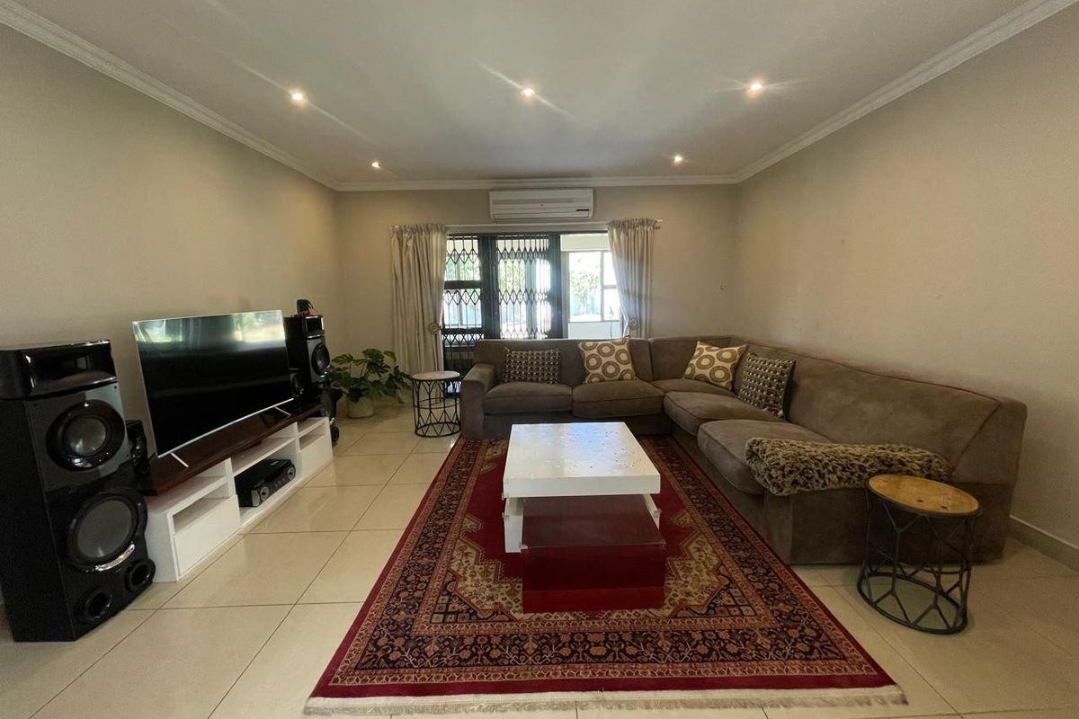 A spacious living room featuring tiled flooring, recessed downlighting, and a wall-mounted split-system air conditioner, providing a comfortable and functional family space.