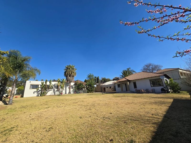 A spacious rear garden view featuring a large lawn area, mature trees, and the rear elevation of the house with tiled roofing.