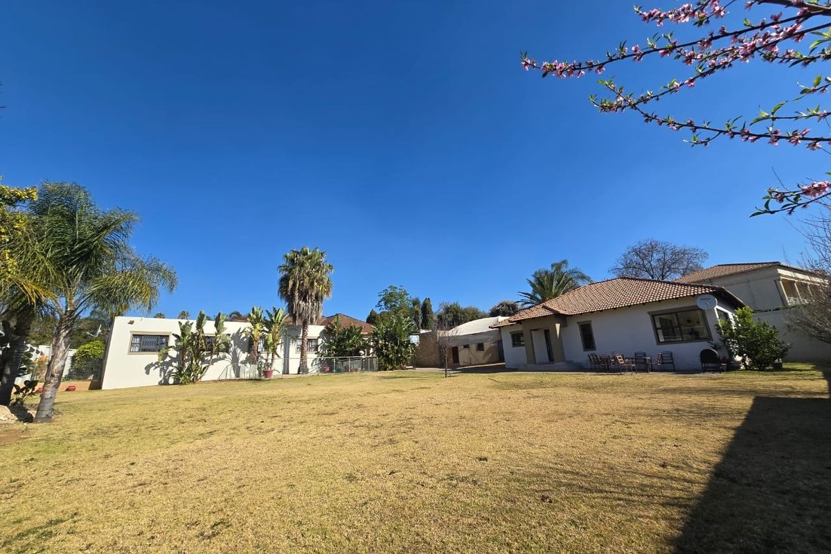 A spacious rear garden view featuring a large lawn area, mature trees, and the rear elevation of the house with tiled roofing.