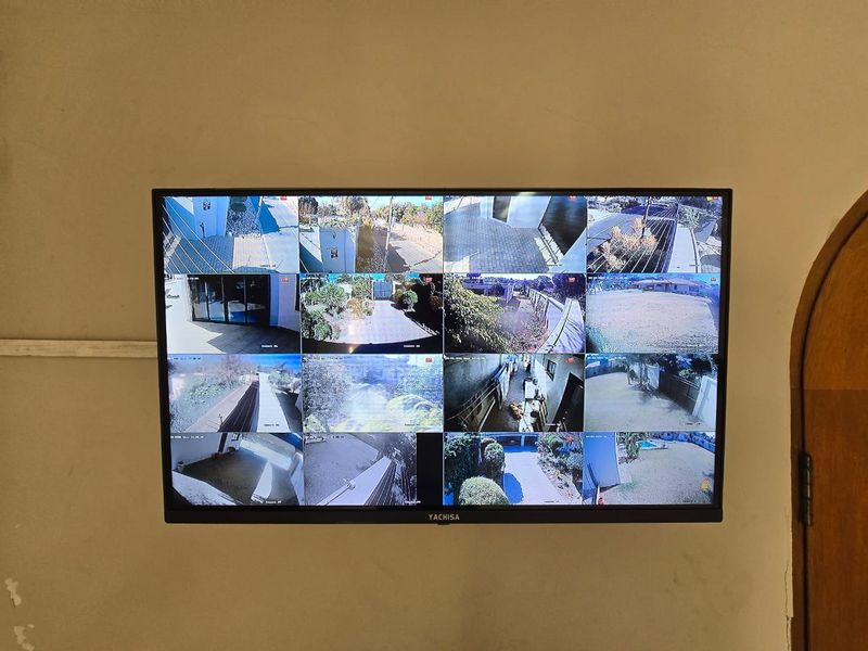 A wall-mounted security monitor displaying multiple camera feeds of the property exterior.