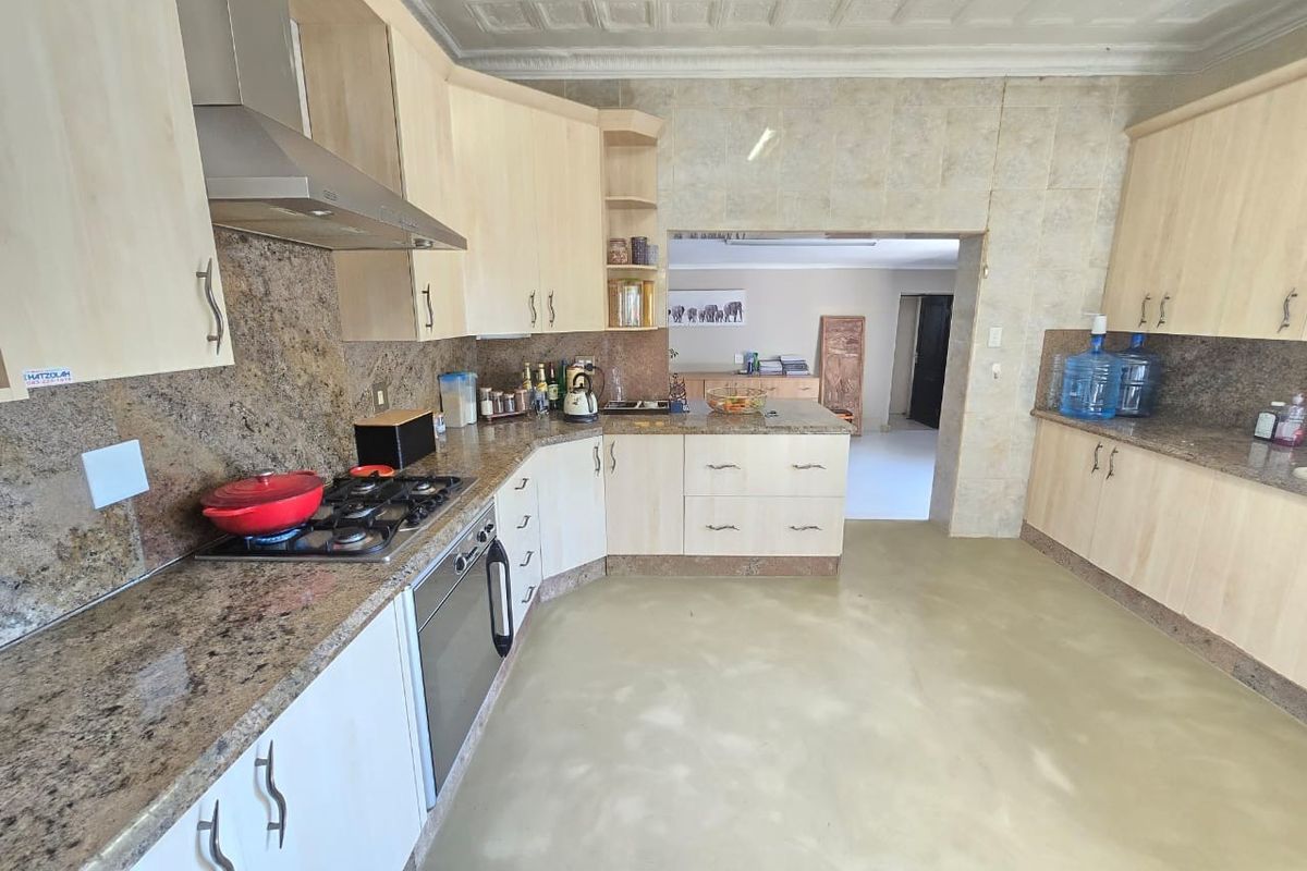 A functional kitchen featuring granite countertops, built-in gas hob, oven, stainless steel extractor fan, and light wood cabinetry with a decorative pressed metal ceiling.