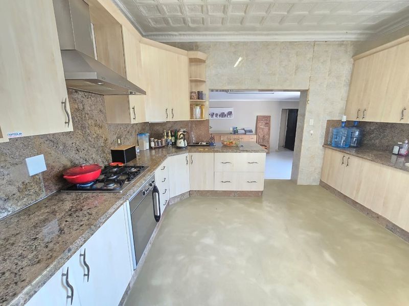 A functional kitchen featuring granite countertops, built-in gas hob, oven, stainless steel extractor fan, and light wood cabinetry with a decorative pressed metal ceiling.