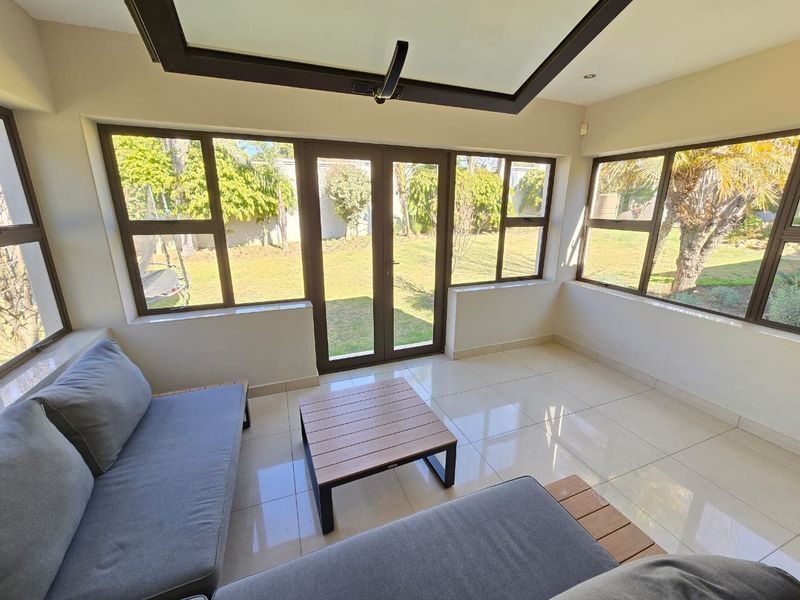 Bright sunroom or enclosed patio featuring large aluminium-framed windows, tiled flooring, and a skylight, offering direct access to the garden.