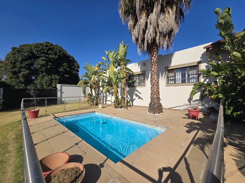 Outdoor pool area featuring a tiled surround, glass balustrade, and established garden landscaping against the rear building elevation.