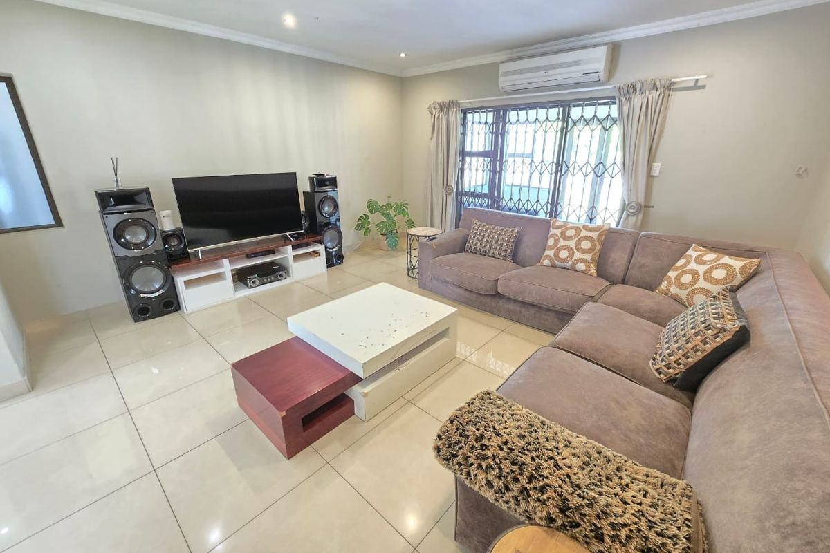 A well-maintained living room featuring large format floor tiles, recessed lighting, and a wall-mounted split-system air conditioner.