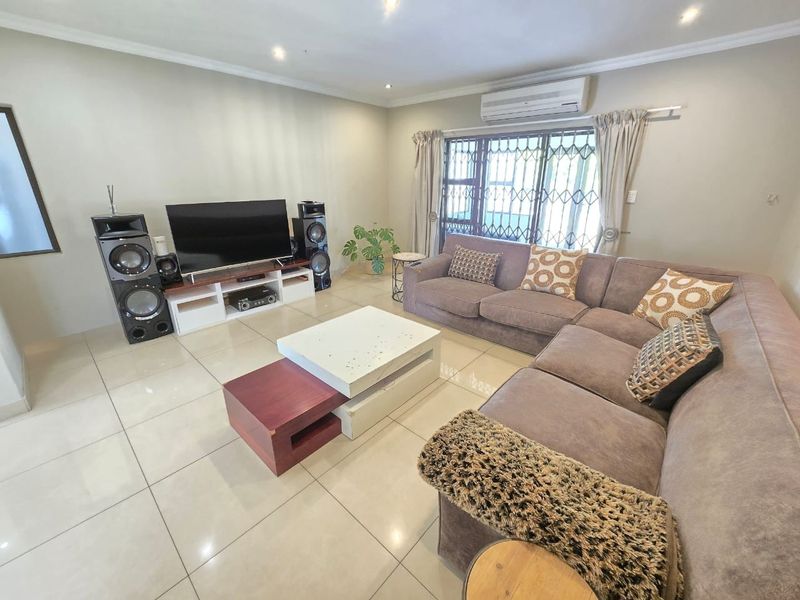 A well-maintained living room featuring large format floor tiles, recessed lighting, and a wall-mounted split-system air conditioner.