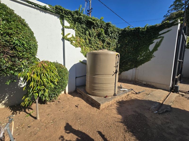 Rear exterior area featuring a water storage tank mounted on a concrete plinth against a perimeter wall with climbing vegetation.