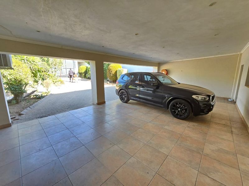 A spacious covered carport or garage area featuring tiled flooring and recessed ceiling lighting, providing sheltered parking space.