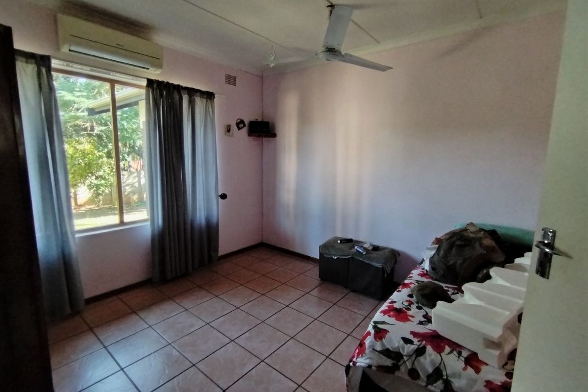 A bedroom featuring tiled flooring, a ceiling fan, and a wall-mounted split-system air conditioning unit.