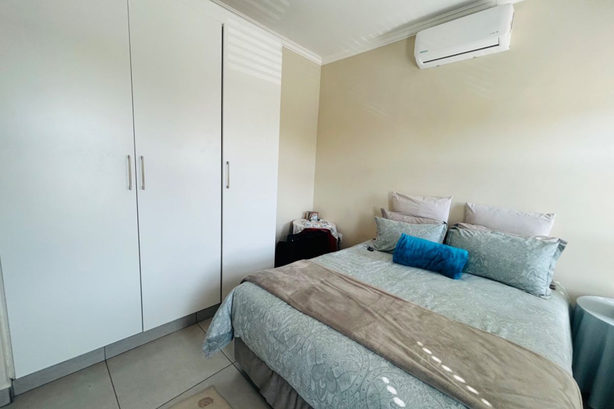 A well-maintained bedroom featuring built-in cupboards, tiled flooring, and a wall-mounted split-system air conditioning unit.