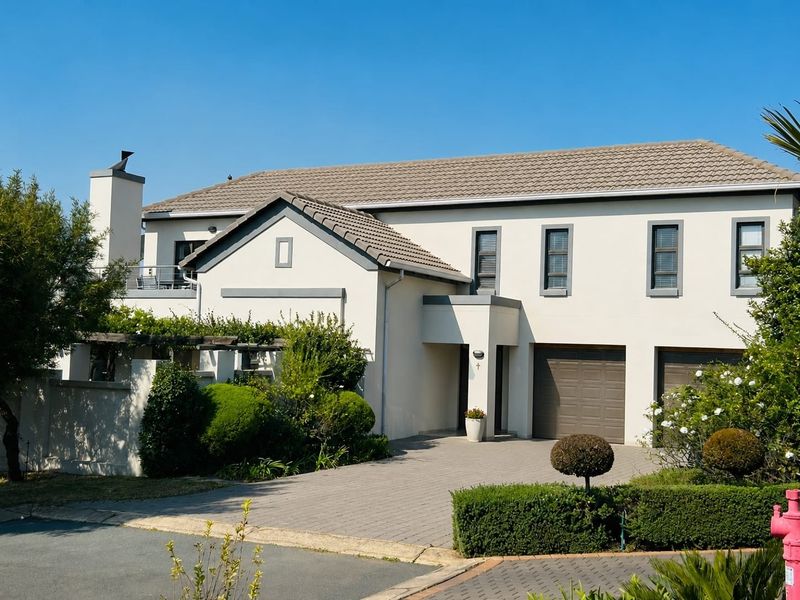 A well-maintained double-storey residential home featuring a paved driveway, double garage, and an upper-level balcony with a chimney.