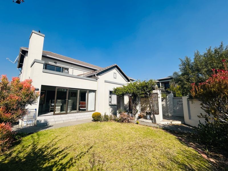 Rear view of the house featuring a paved patio area, sliding glass doors, a chimney, and a well-maintained garden with a pergola.