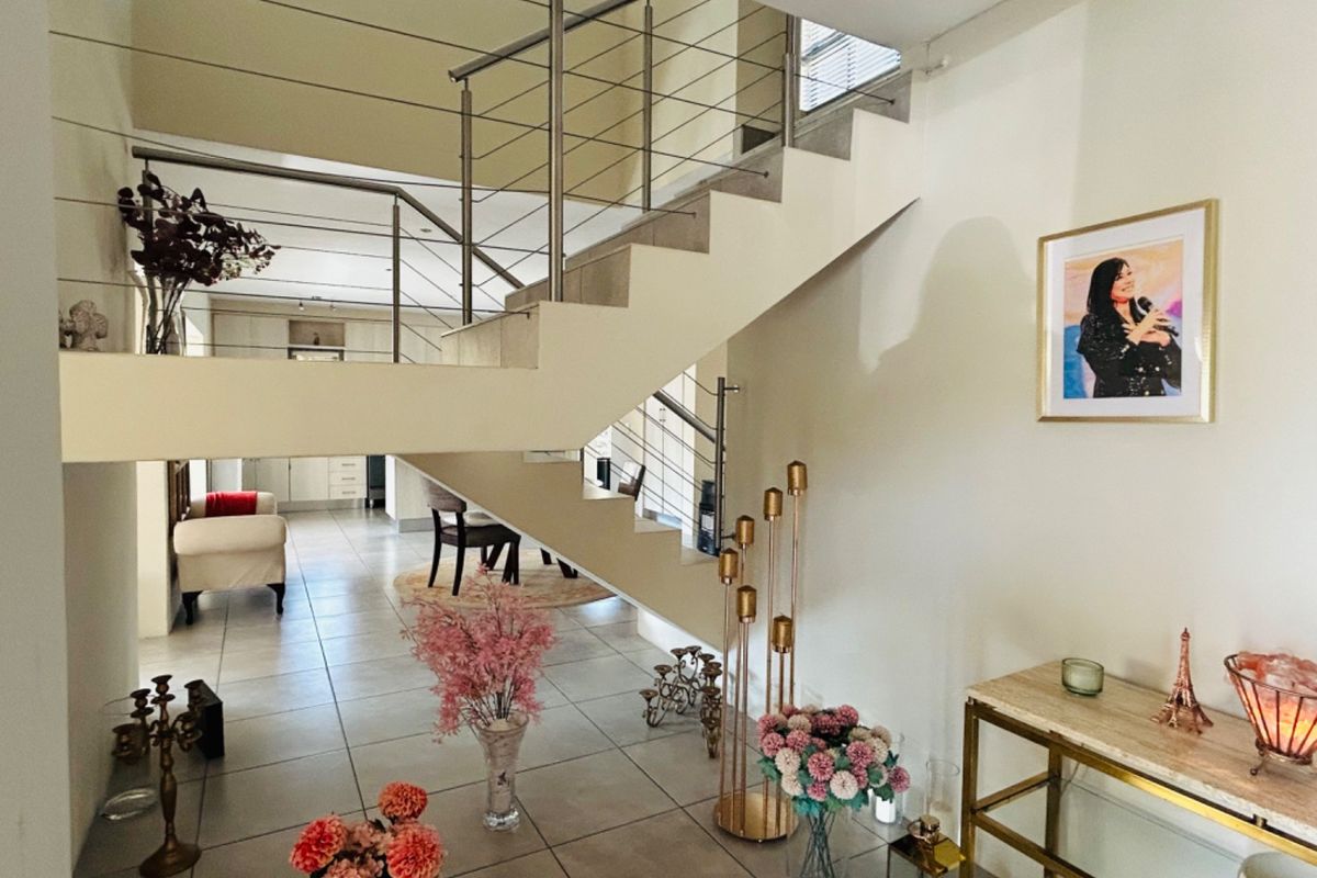 Open-plan living area featuring a modern staircase with stainless steel balustrades and neutral tiled flooring throughout.
