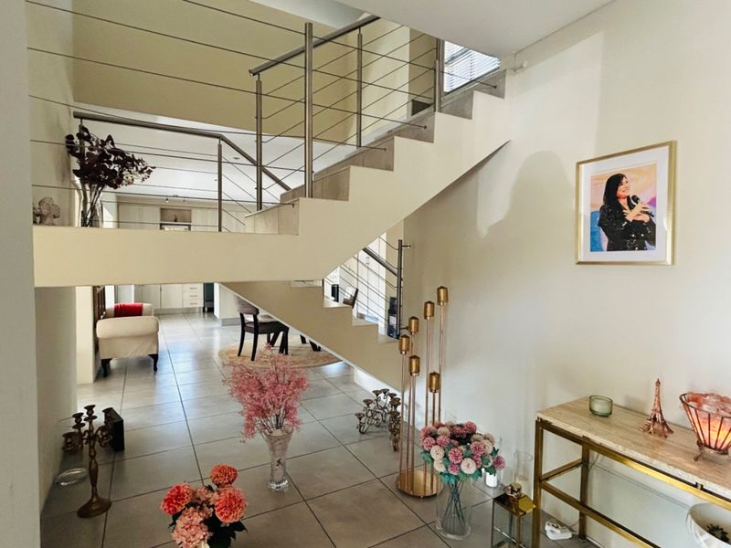 Open-plan living area featuring a modern staircase with stainless steel balustrades and neutral tiled flooring throughout.
