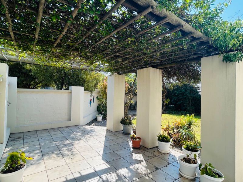 A covered patio area featuring a timber pergola, tiled flooring, and masonry pillars, overlooking a private garden space.