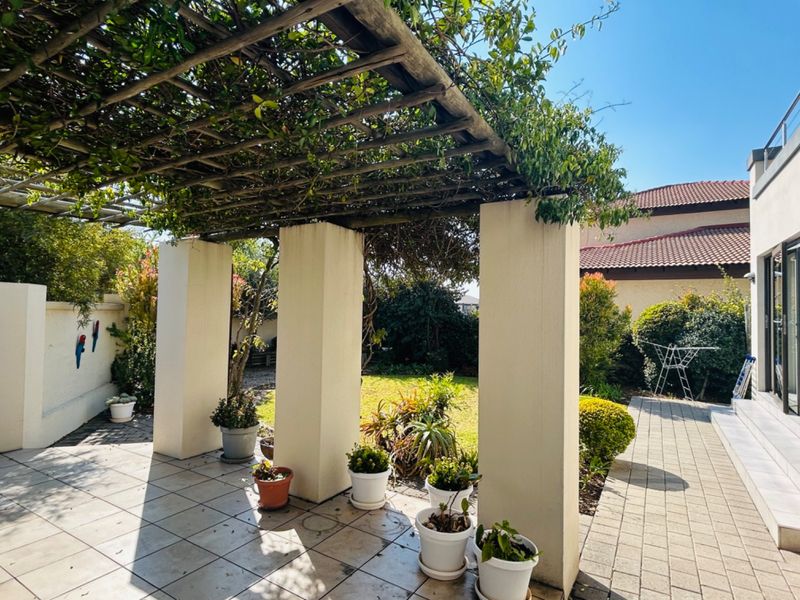 A covered patio area featuring a timber pergola structure, tiled flooring, and masonry pillars, overlooking a private garden space.