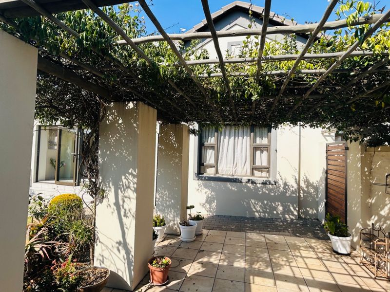 A covered patio area featuring a timber pergola, tiled flooring, and masonry pillars, providing a shaded outdoor space adjacent to the main dwelling.