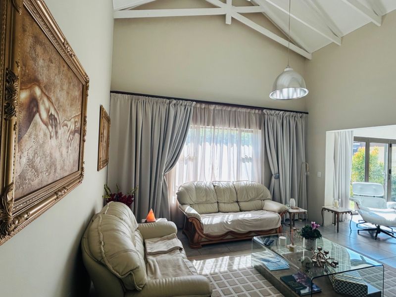 Spacious living room featuring a high vaulted ceiling with exposed rafters, tiled flooring, and large sliding glass doors providing natural light and garden access.