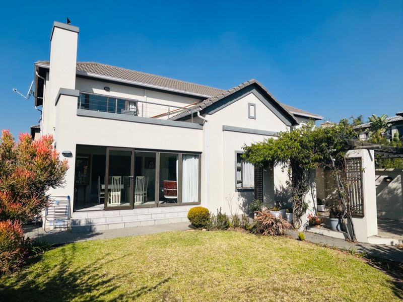 Rear view of a two-story house featuring a paved patio, a balcony, and a well-maintained garden area.