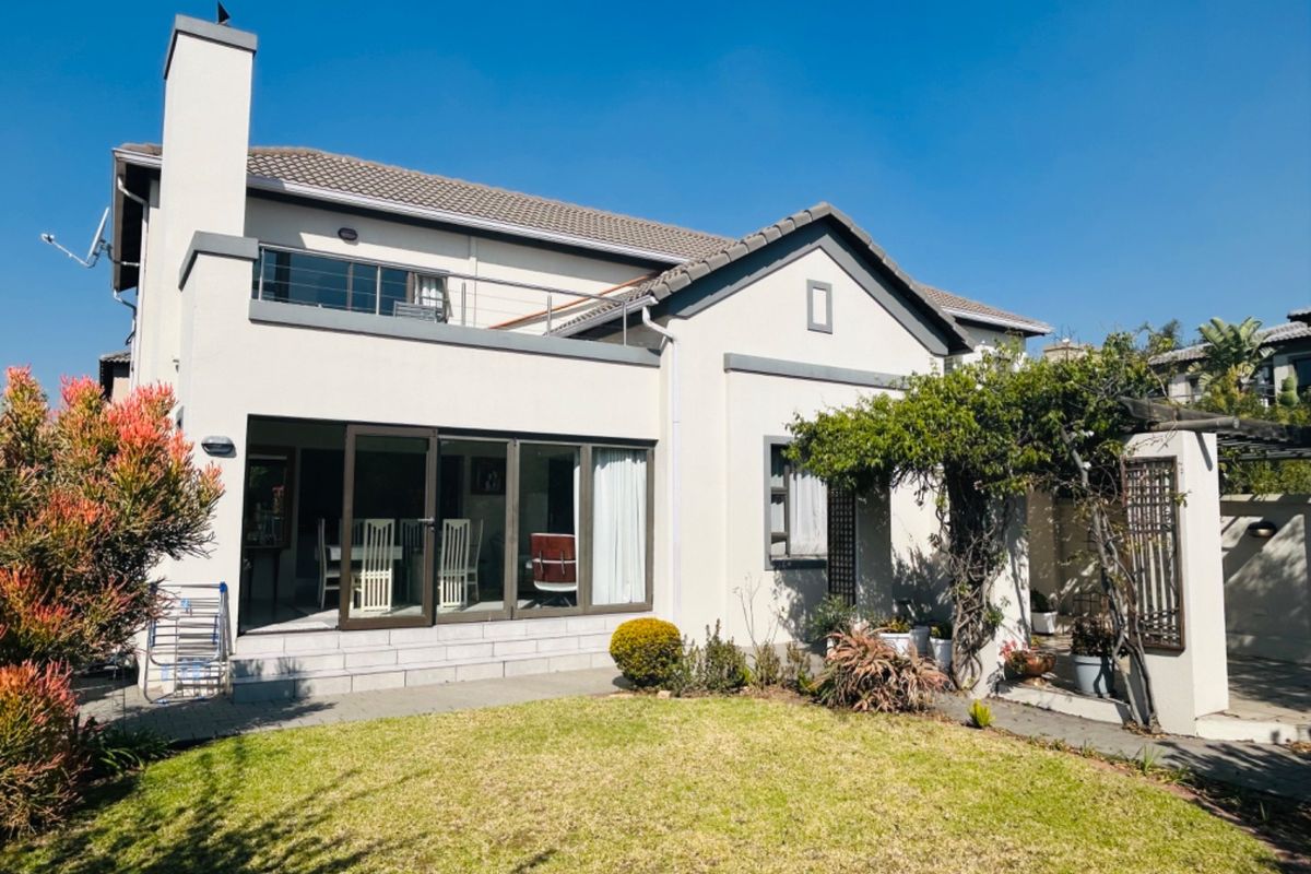 Rear view of a two-story house featuring a paved patio, a balcony, and a well-maintained garden area.