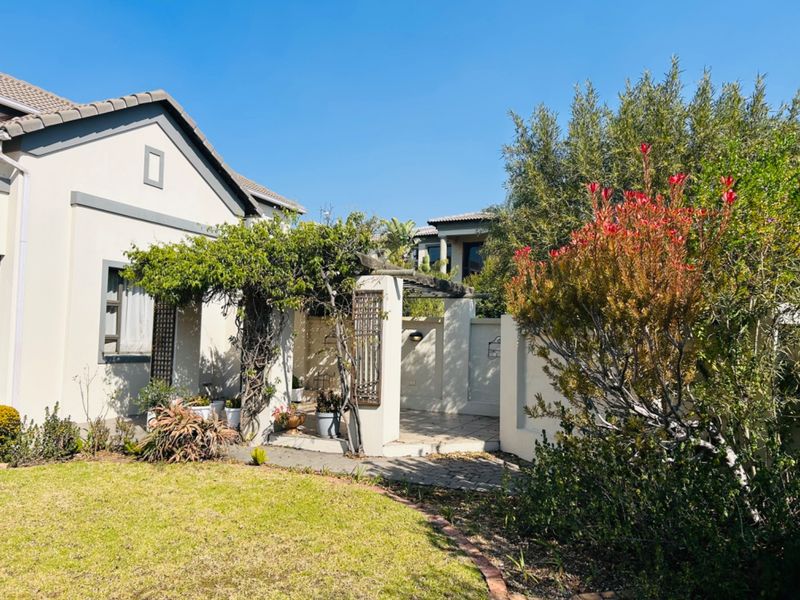 A well-maintained rear exterior view featuring a paved patio area with a pergola, surrounded by a landscaped garden and boundary walls.