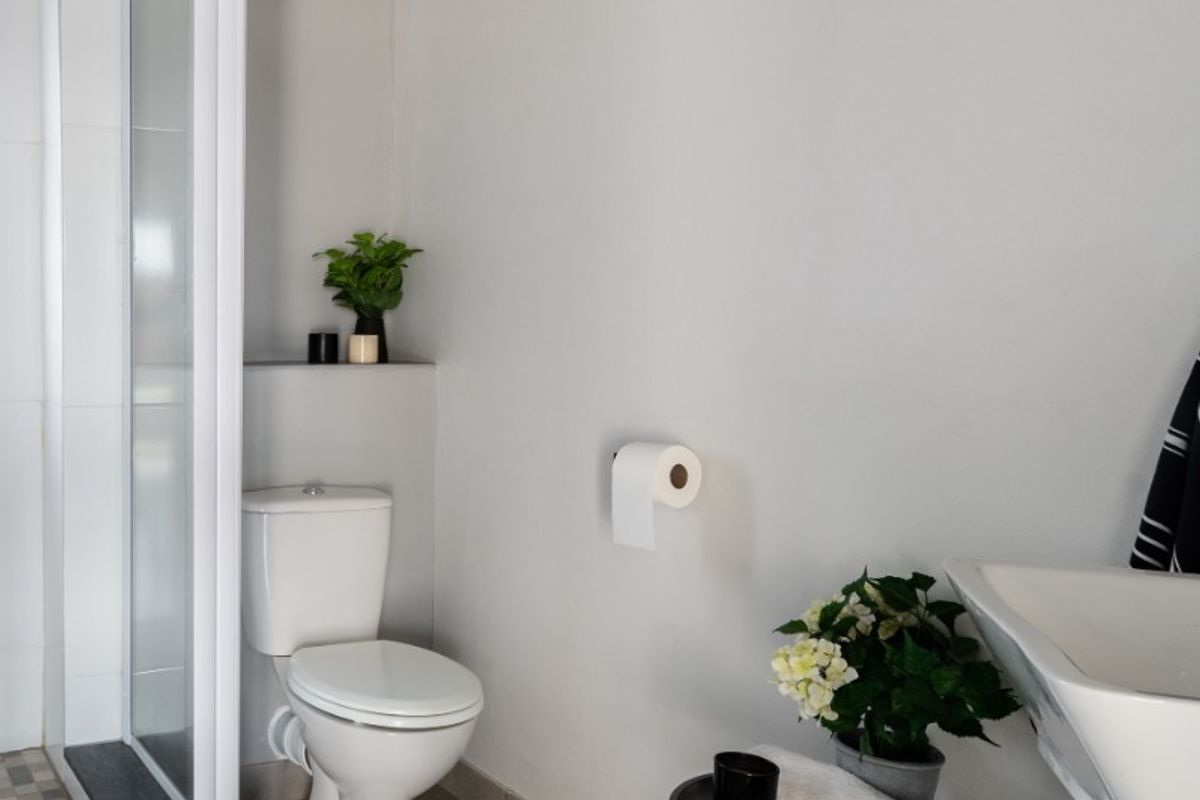 A modern bathroom featuring a glass-enclosed shower, a white toilet, and a wall-mounted basin with neutral floor tiling.
