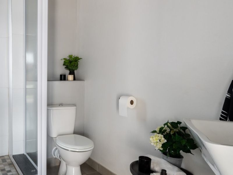A modern bathroom featuring a glass-enclosed shower, a white toilet, and a wall-mounted basin with neutral floor tiling.