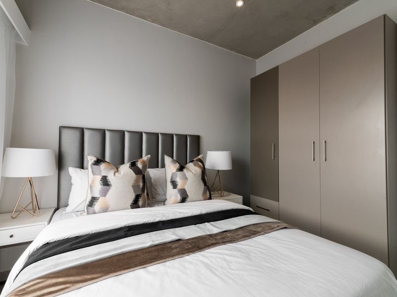 Modern bedroom featuring a sleek exposed concrete ceiling, recessed lighting, and integrated floor-to-ceiling built-in cupboards with a contemporary finish.