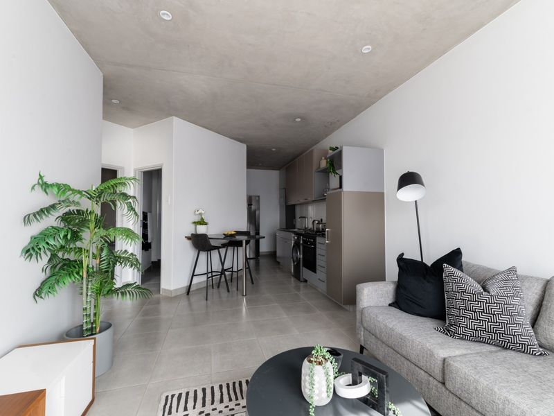 Modern open-plan living area featuring a sleek kitchen with built-in cabinetry, tiled flooring, and a contemporary exposed concrete ceiling.