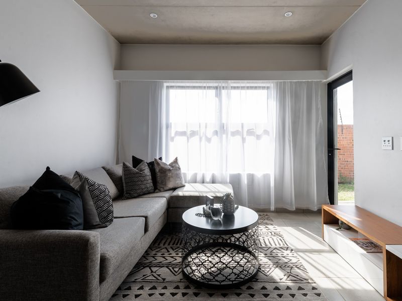 A bright and modern living room featuring tiled flooring, recessed ceiling lights, and direct access to an outdoor area through a glass door.