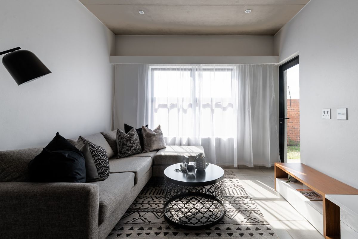 A bright and modern living room featuring tiled flooring, recessed ceiling lights, and direct access to an outdoor area through a glass door.
