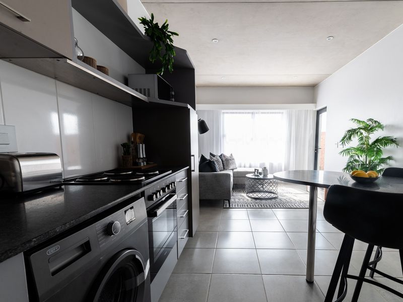 Modern open-plan apartment featuring a sleek kitchen with built-in appliances, tiled flooring, and a seamless transition to the living area with natural light.