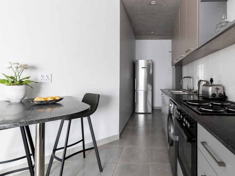 Modern galley-style kitchen featuring sleek cabinetry, granite countertops, integrated appliances, and a contemporary exposed concrete ceiling, complemented by tiled flooring.