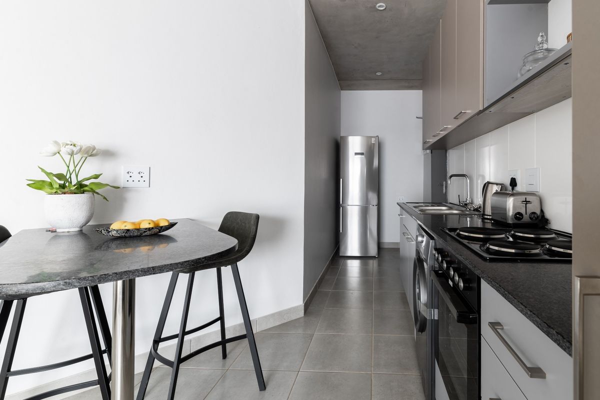 Modern galley-style kitchen featuring sleek cabinetry, granite countertops, integrated appliances, and a contemporary exposed concrete ceiling, complemented by tiled flooring.
