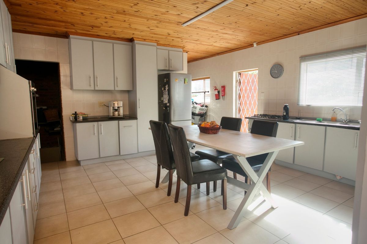 Spacious kitchen featuring light grey cabinetry, tiled flooring, a timber ceiling, and integrated cooking appliances with an adjacent dining area.