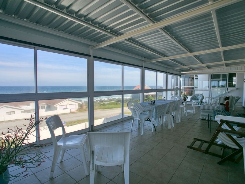 Spacious enclosed patio featuring tiled flooring and expansive glass windows offering panoramic ocean views, perfect for relaxed coastal living.