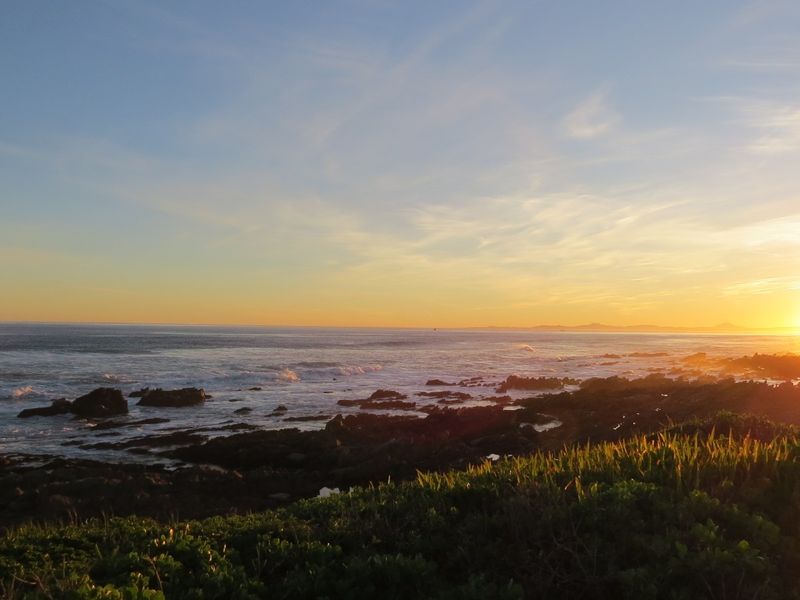 A scenic coastal view featuring a rocky shoreline and ocean horizon at sunset.