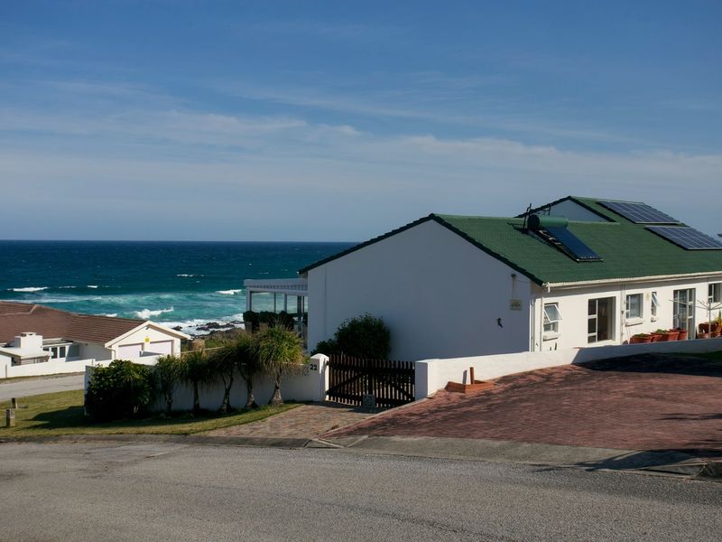 A coastal property featuring a metal roof with integrated solar panels and a solar water heater, complemented by a paved driveway and boundary wall.